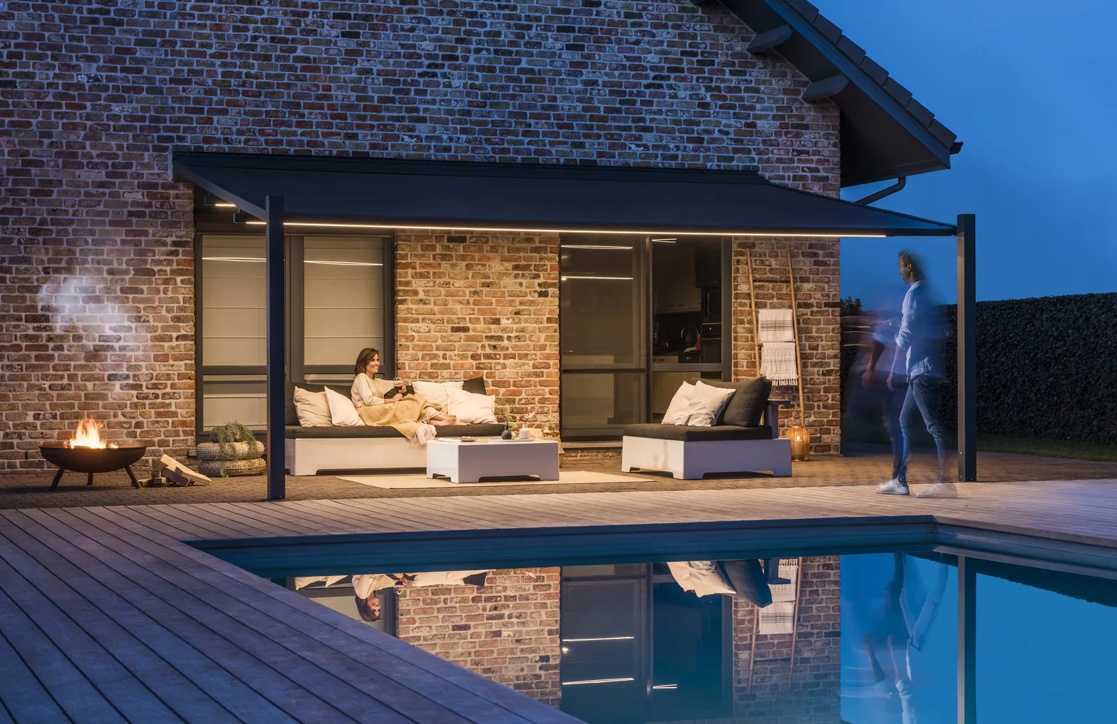 Pergola-Markise über einer beleuchteten Lounge am Pool, Abend